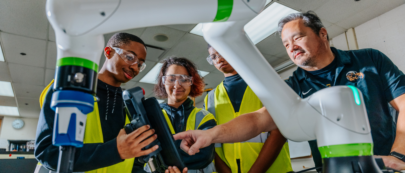 Instructor demonstrating robotic arm with three high school students