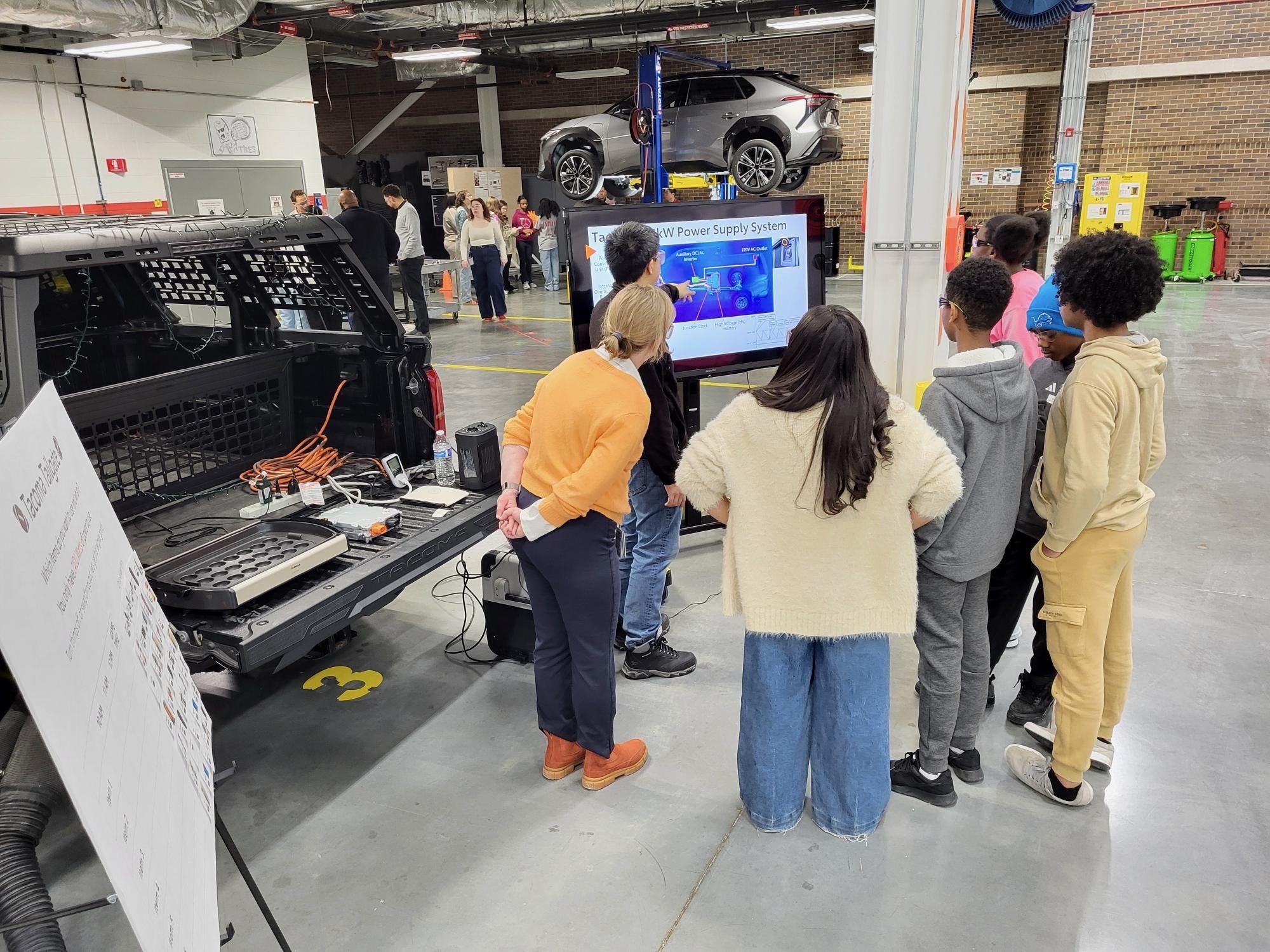 Students stand around a TV monitor to learn about automotive technology